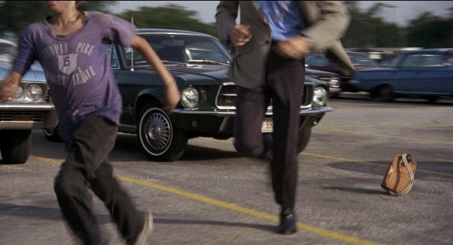 Wide shot frame from Medium Cool — car, shirt, bag