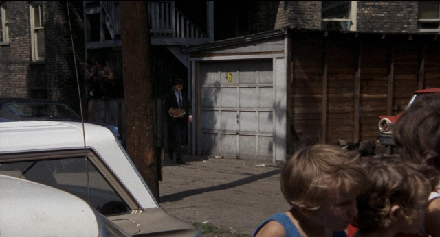 Wide shot frame from Medium Cool — standing, door, street