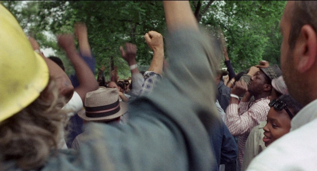 Wide shot frame from Medium Cool — standing, hat, person