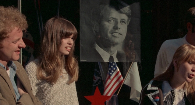 Medium shot frame from Medium Cool — standing, dialogue, flag