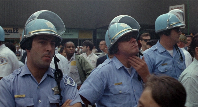 Wide shot frame from Medium Cool — standing, dialogue, hat