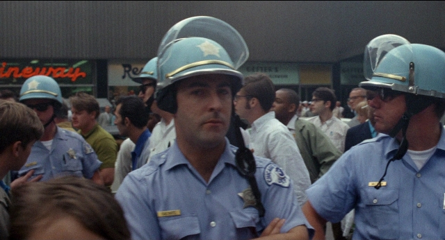 Frame from Medium Cool — standing, hat, person