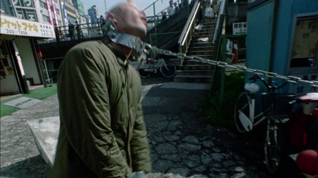 Wide shot frame from 964 Pinocchio — standing, street, hand