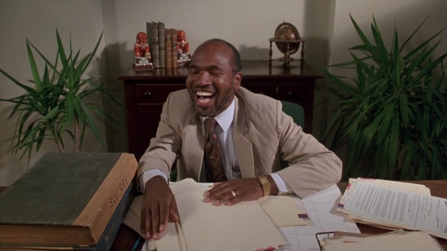 Wide shot frame from Cool Runnings — sitting, book, room