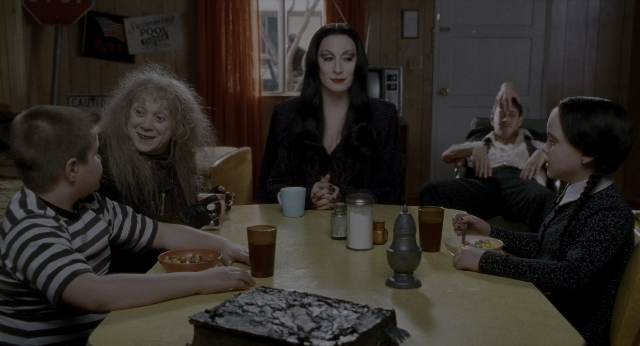 Wide shot frame from The Addams Family — sitting, room, table