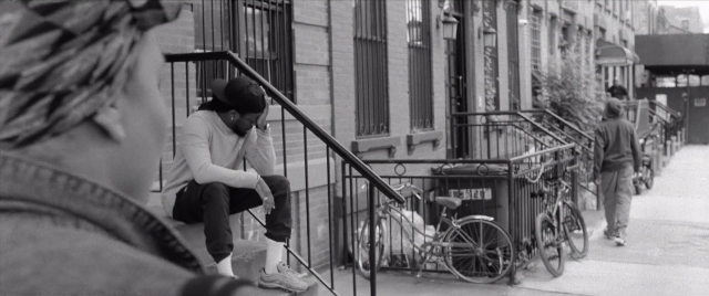 Wide shot frame from The Forty-Year-Old Version — sitting, walking, phone