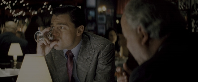 Wide shot frame from The Wolf of Wall Street — sitting, table, hand