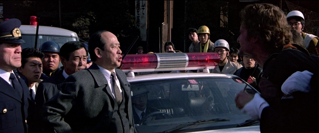Close-up frame from Black Rain — dialogue, car, suit