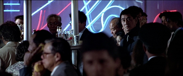 Wide shot frame from Black Rain — sitting, standing, dialogue