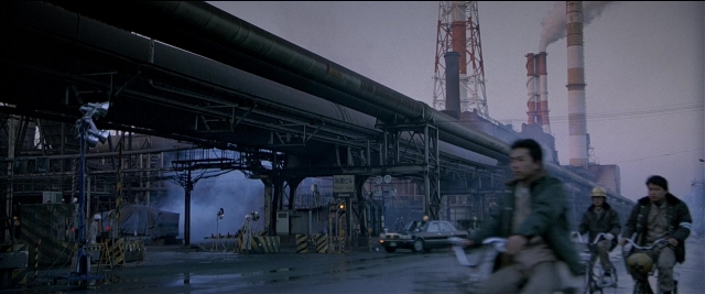 Wide shot frame from Black Rain — street, bicycle, smoke