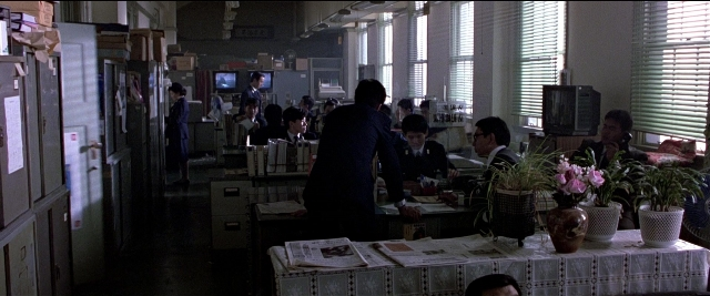 Wide shot frame from Black Rain — sitting, book, room