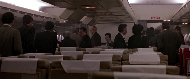 Wide shot frame from Black Rain — sitting, standing, suit