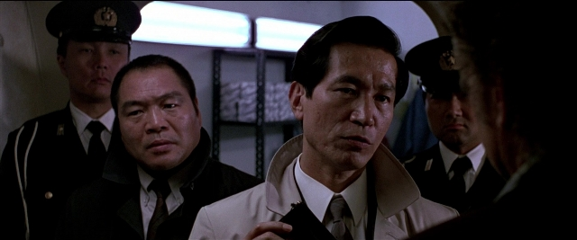 Medium shot frame from Black Rain — standing, room, hat