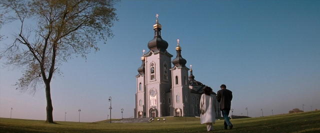 Wide shot frame from In the Mouth of Madness — walking, tower, clock