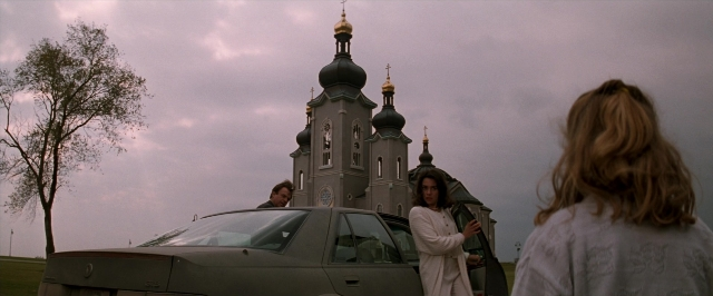 Wide shot frame from In the Mouth of Madness — standing, car, tower