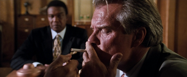 Wide shot frame from In the Mouth of Madness — sitting, room, table