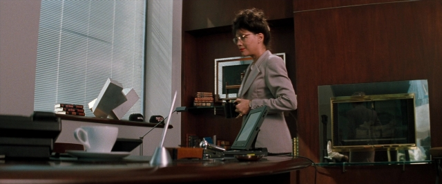 Wide shot frame from In the Mouth of Madness — desk, standing, hand