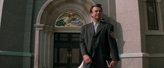 Wide shot frame from In the Mouth of Madness — standing, door, hand