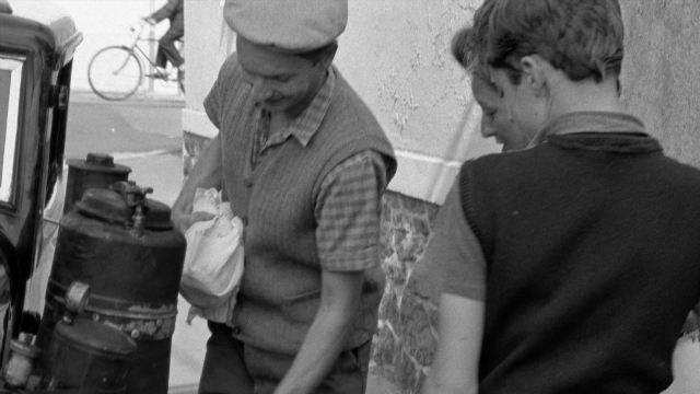 Wide shot frame from In the Mouth of Madness — standing, street, hat