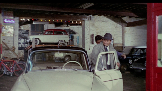 Wide shot frame from In the Mouth of Madness — standing, door, hat