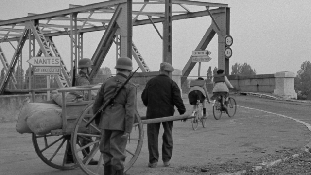 Wide shot frame from In the Mouth of Madness — standing, walking, hat