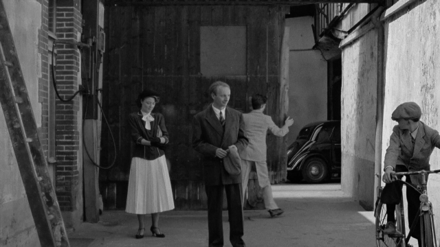 Wide shot frame from In the Mouth of Madness — standing, door, hat