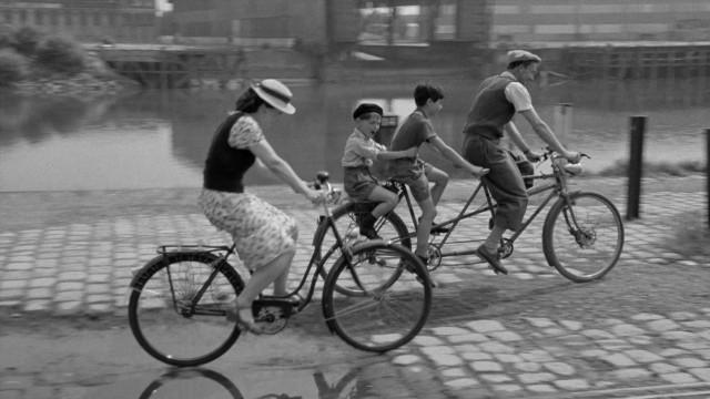 Wide shot frame from In the Mouth of Madness — sitting, street, hat