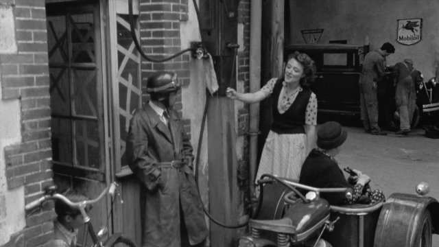 Wide shot frame from In the Mouth of Madness — sitting, standing, hat