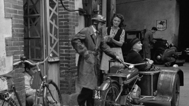 Wide shot frame from In the Mouth of Madness — sitting, standing, street