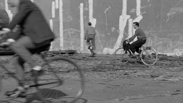Wide shot frame from In the Mouth of Madness — dialogue, street, suit