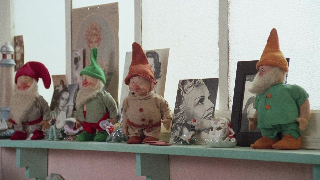 Wide shot frame from In the Mouth of Madness — standing, hat, dress