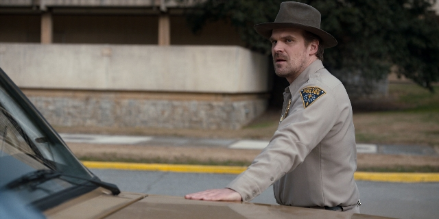 Wide shot frame from Stranger Things — standing, street, hat