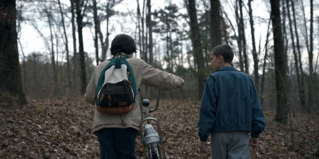 Wide shot frame from Stranger Things — walking, bicycle, jacket