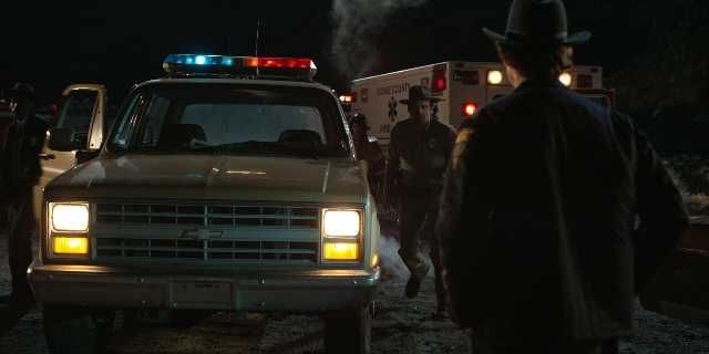 Wide shot frame from Stranger Things — standing, street, fire