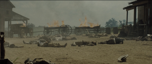 Wide shot frame from The Magnificent Seven — fire, cart, smoke