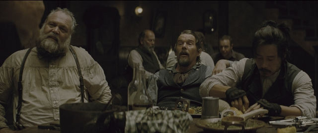 Wide shot frame from The Magnificent Seven — sitting, plate, table