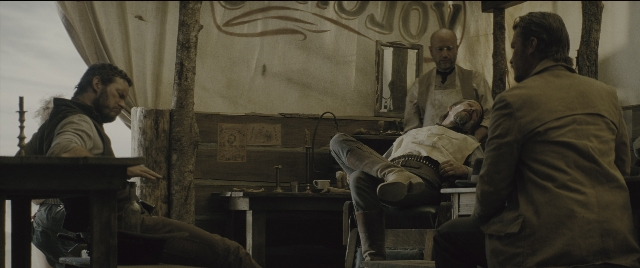 Wide shot frame from The Magnificent Seven — sitting, book, standing