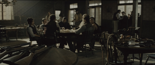 Wide shot frame from The Magnificent Seven — sitting, standing, room
