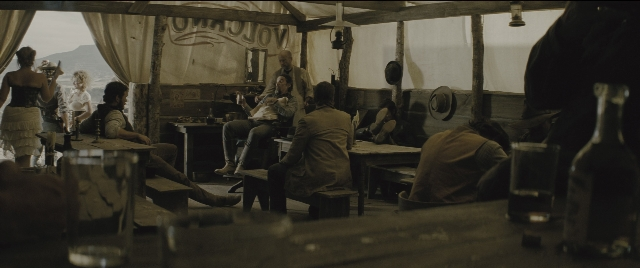 Wide shot frame from The Magnificent Seven — sitting, standing, table