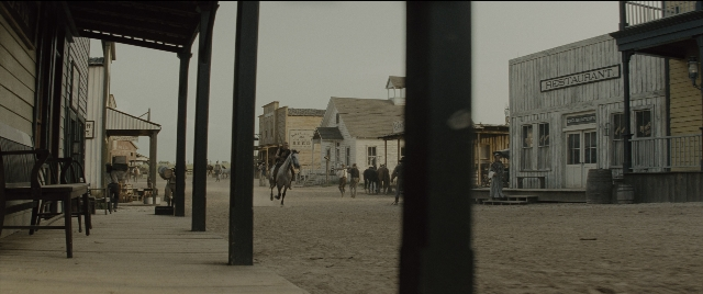 Wide shot frame from The Magnificent Seven — walking, table, street
