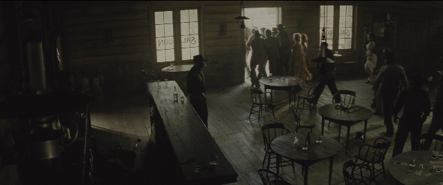 Wide shot frame from The Magnificent Seven — standing, room, table