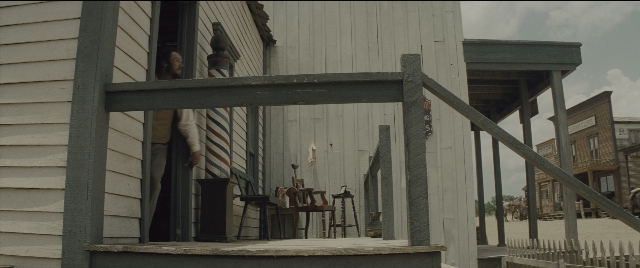Wide shot frame from The Magnificent Seven — standing, table, suit