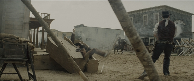 Wide shot frame from The Magnificent Seven — standing, horse, train