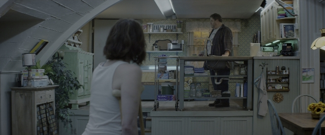 Wide shot frame from 10 Cloverfield Lane — standing, room, table