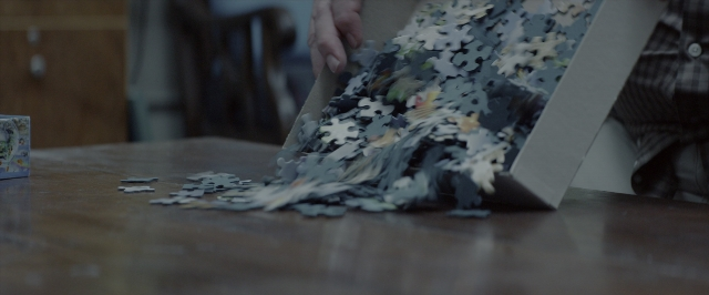 Wide shot frame from 10 Cloverfield Lane — room, table, hand