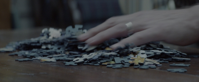 Wide shot frame from 10 Cloverfield Lane — room, table, hand