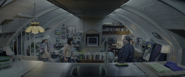 Wide shot frame from 10 Cloverfield Lane — standing, room, table