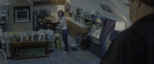 Wide shot frame from 10 Cloverfield Lane — sitting, book, standing