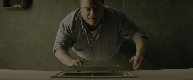Wide shot frame from 10 Cloverfield Lane — room, table, shirt