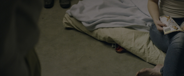 Wide shot frame from 10 Cloverfield Lane — sitting, book, room